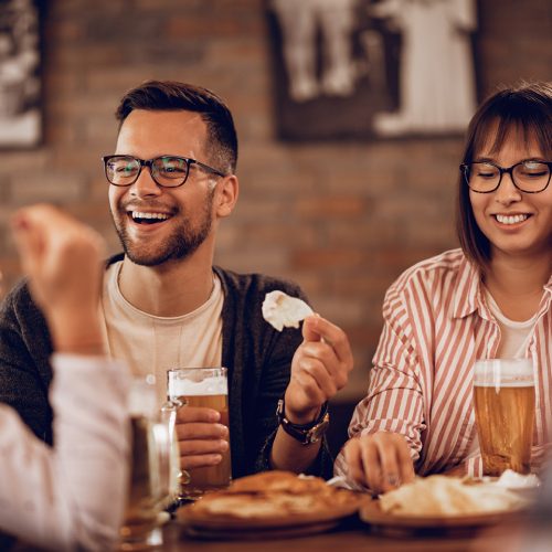 Happy couple enjoying with friends while drinking beer and communicating  in a tavern.